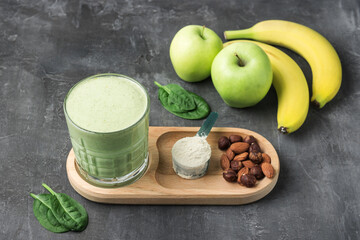 Green detox smoothie in a glass, measuring spoon with protein powder, blended vegetarian drink from...