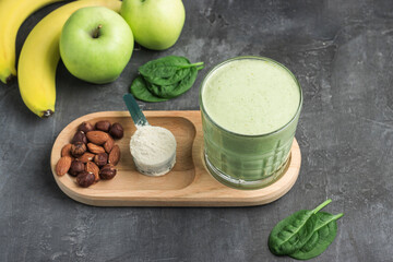Green detox smoothie in a glass, measuring spoon with protein powder, blended vegetarian drink from...