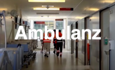 Ambulanz Schriftzug, im Hintergrund ein Gang der Notaufnahme im Krankenhaus mit Betten, Lichtern...