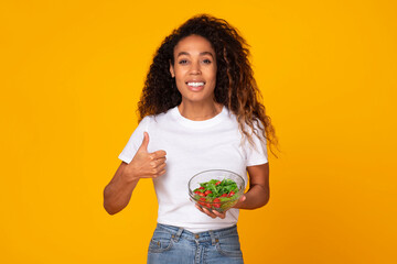 black woman holding bowl of salad gesturing thumbs up, studio