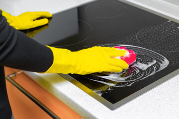 woman in rubber gloves washes the hob in the kitchen.