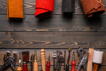Leather and leather craft work tools instruments on the old wooden workbench flat lay background with copy space. Top view.