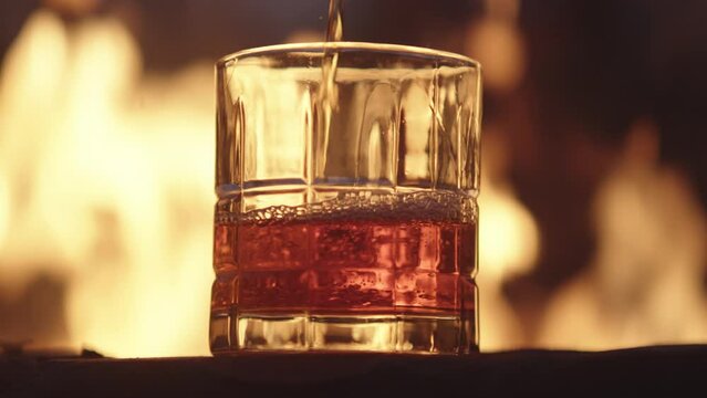 Glass of whiskey being poured in the outdoors in front of a large fire