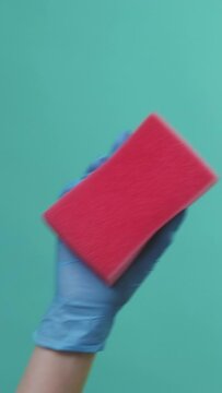 Vertical video. Cleaning equipment. Home hygiene. Housekeeper in protective gloves washing surface with red sponge tool in hand isolated on green background.