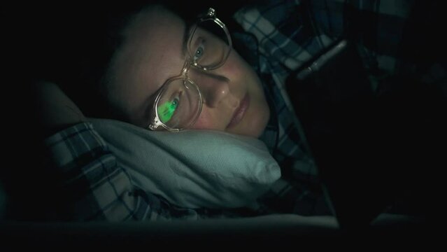 Night phone. Middle-aged girl in sleep pajamas, tired looking tired man not sleeping in the bedroom. Camera in motion, modern girl holding phone in hands at night in the process of studying, insomnia