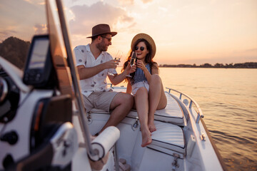 Couple having fun drinking champagne and sailing to the sunset on a boat