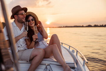 Couple hugging and drinking champagne while sailing to the sunset on a boat
