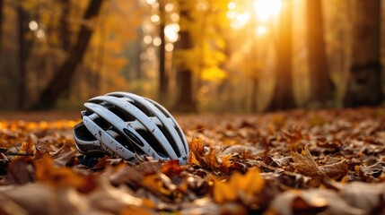 A bicycle helmet rests on the forest floor amidst fallen autumn leaves, with the warm, soft light of the setting sun filtering through the trees in the background - obrazy, fototapety, plakaty