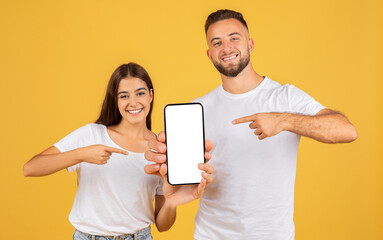 Smiling young woman and man in white shirts holding and pointing at a smartphone