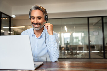 Happy senior latin Hispanic man in wearing headphones, helping as callcenter consult assistant. Smiling mature 40s years old mixed race businessman holding video call with clients partners. Copy space