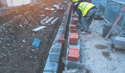 Hard working bricklayer laying concrete blocks on top of concrete foundation on new residential...