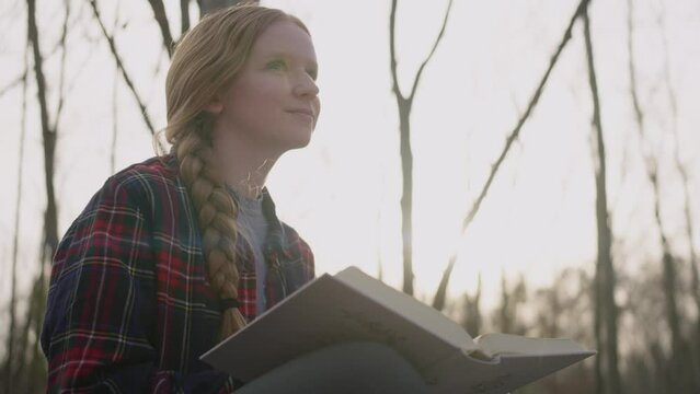 Smiling young woman reading her bible, writing notes, and admiring nature