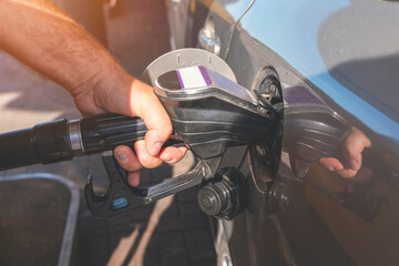 A man filling fuel tank of his car with diesel fuel at the petrol station close up, as cost of fuel...