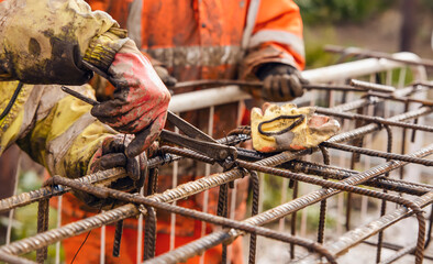 A worker uses steel tying wire to fasten steel rods to reinforcement bars close-up. Reinforced concrete structures - making a steel reinforcing cage for concrete beam