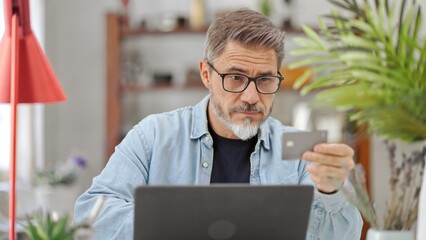 Casual mid adult man with laptop computer at desk in home, banking online shopping on internet...