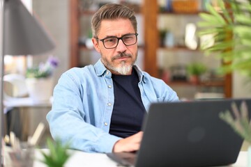 Casual mid adult man with laptop computer at desk in home office, banking online, remote working....