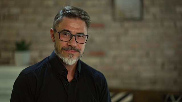 Portrait Of Happy, Confident Older Man At Home Looking At Camera Smiling. Mature Age, Middle Age, Mid Adult Casual Guy In 50s, Bearded, Gray Hair, Wearing Glasses.