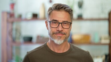 Portrait of happy, confident older man at home looking at camera smiling. Mature age, middle age, mid adult casual guy in 50s, bearded, gray hair, wearing glasses.