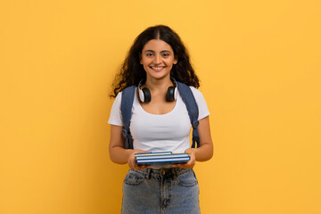 Happy cute young indian woman student posing on yellow background - obrazy, fototapety, plakaty