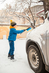 Cute little boy is helping his father brush the snow from the car. Snow removal from the car...