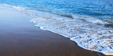 Seascape. Sandy beach sea shore with blue wave and white foam. Sea ​​waves on the sand on the beach. Blue sea waves on the beach for background. Abstract beach sand and soft wave background
