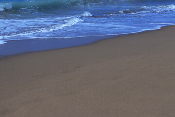 Seascape. Sandy beach sea shore with blue wave and white foam. Sea ​​waves on the sand on the beach. Blue sea waves on the beach for background. Abstract beach sand and soft wave background