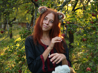 Selfie portraits of a red-haired woman with a fluffy tail and ears in the summer outdoors in an apple orchard. Cosplay for Holo, the wise she-wolf from the anime Spice and the wolf in ethnic clothes.