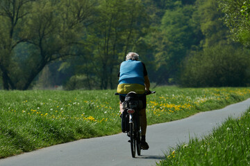 Mann in kurzer Hose und blauer Weste fährt auf einem Tourenrad durch blühende Wiesen auf dem...