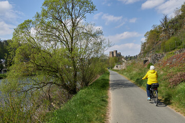 Frau in gelber Steppjacke fährt auf einem Tourenrad auf dem asphaltierten Lahn-Radweg oberhalb von...