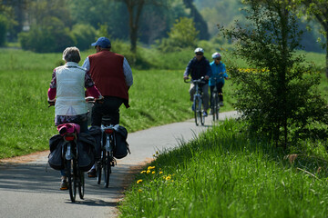 Naklejka premium Älteres Ehepaar mit Tourenrädern fährt durch blühende Wiesen auf einem asphaltierten Radweg