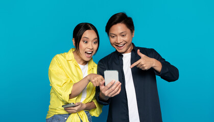 Excited Asian couple interact with a smartphone, the woman holding the device