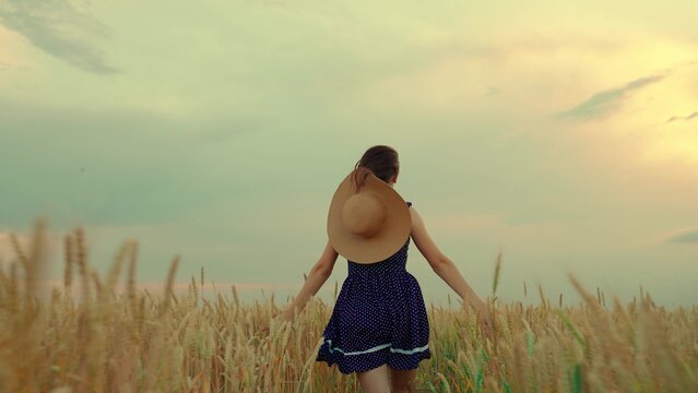Woman farmer run through field, touching ears wheat with hand. Girl in red dress, straw hat walking alone across wheat field. Young girl walk through field with wheat, touching cold ears with hands.