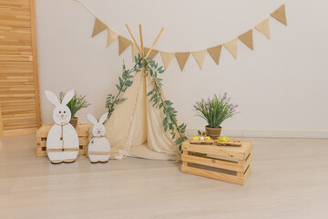 Interior design of easter living room with easter bunny sculptures, garland, plants, wooden boxes,flags garland, tent, wigwam. Home decor.Warm and cozy composition