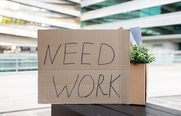 Cardboard sign with 'Need Work' text alongside personal items