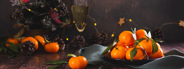Whole tangerines with leaves on a plate on the table in Christmas decorations web banner