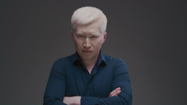 Portrait of an Asian albino guy. Eastern man with a genetic mutation of pigment, white hair. The arms are crossed on the chest. The male is wearing a dark shirt in the studio. Abnormal deviations