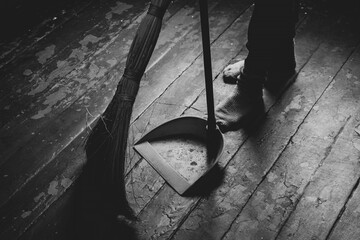 Women's feet on the floor and a broom and dustpan nearby, a girl sweeping the floor of the house,...