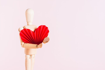 Wooden man holding a big red origami heart on a pink background
