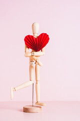 Wooden mannequin with red origami heart on pink background vertical view