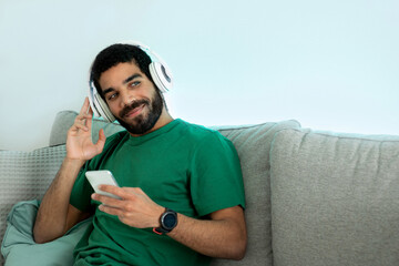 Relaxed young man with a beard and a green shirt, lounging on a gray couch - Powered by Adobe