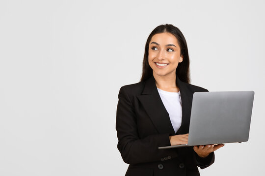 Smiling businesswoman holding laptop against grey background, free space