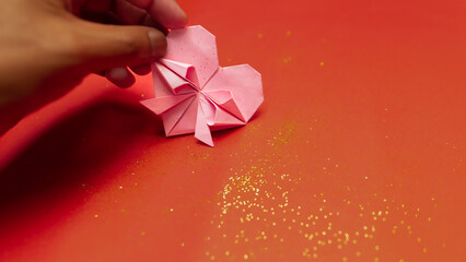 Hand holding paper origami hearts on a red background with golden glitters. Decorations concept for...