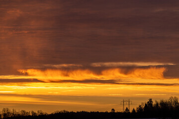 Dark treeline silhouette, power lines and sunrise with updraft wind unusual shaped clouds