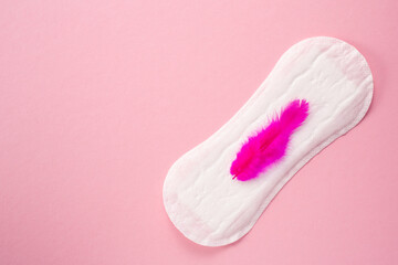 Feminine hygiene pad with red feather on menstrual pad on pink background. First menstrual period...