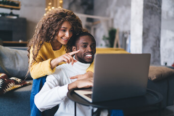 Radiant African-American woman points at laptop computer screen, engaging with smiling man in cozy...