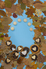 Autumn leaves frame with dry citrus fruits slices of oranges and mandarins and wooden hearts on blue paper background.