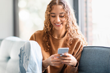 Teen girl websurfing on smartphone sitting on couch at home