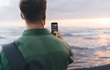 Anonymous man taking photo of sunset over sea