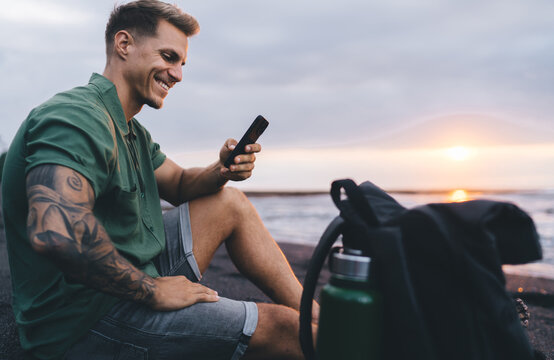 Cheerful young man using smartphone near sea