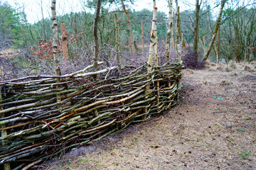 Natural fence made out of branches and logs in woodland 